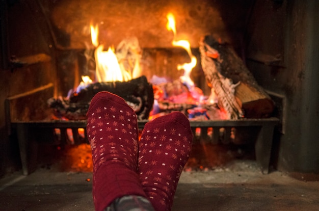 Warmte voeten in rode sokken bij de open haard thuis. Kerstavond thuis.