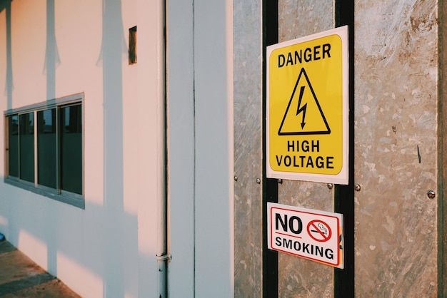 Warning danger high voltage sign and no smoking label on steel pipe cover outside of building