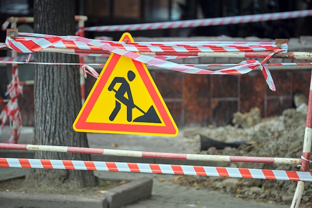 Photo warning roadworks sign and safety barrier on city street during maintenance repair work