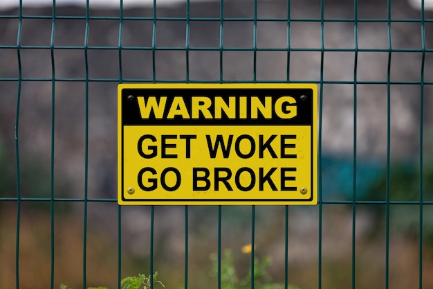 Warning sign on a fence stating in Warning Get woke go broke