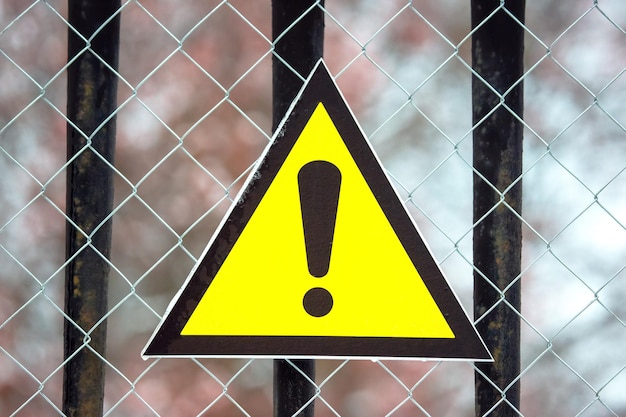 Photo warning sign in the form of a triangle on a metal mesh fence