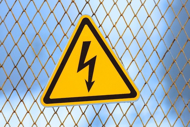 Warning sign, yellow triangle with lightning on a fence made of metal mesh. High quality photo