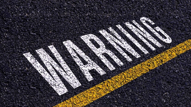 Warning written and yellow line on the road in middle of the asphalt road Warning word on street