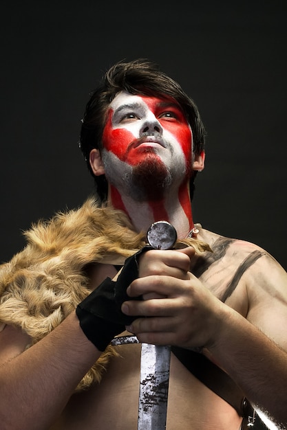 Warrior in war paint, holding a sword with both hands, and pray fixing his eyes to the sky