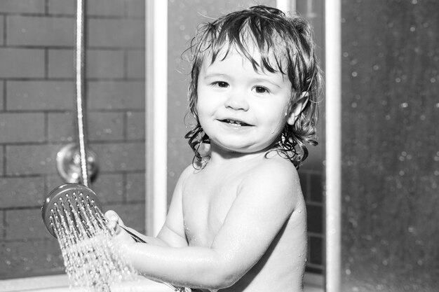 Wash infant hygiene and health care. Funny baby kid bathed in foam and washing in bathtub at home.