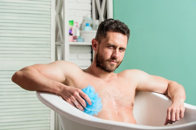 Wash off foam with water carefully Sex and relaxation concept Macho naked in bathtub man wash muscular body with foam sponge macho enjoying bath Sexy man in bathroom Looking good