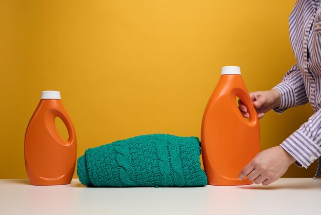 Foto abbigliamento lavato piegato e grandi bottiglie di plastica arancione con detergente liquido in piedi su un bianco