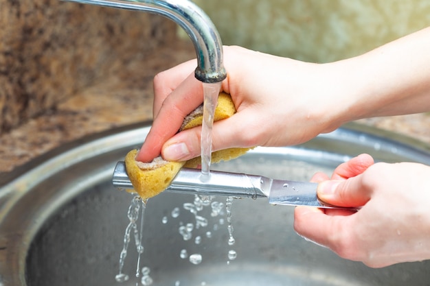 Washing cutlery under running water in the kitchen, hands close up