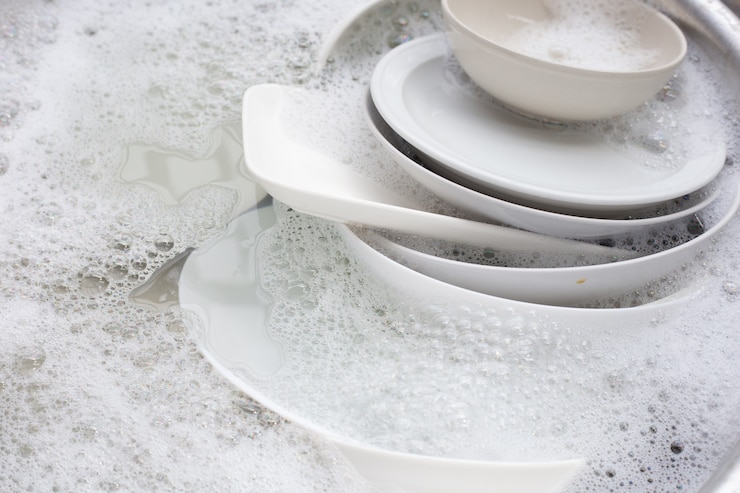Photo washing dishes, close up of utensils soaking in kitchen sink.