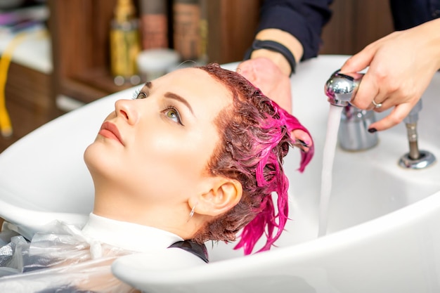 Washing dyed female hair A young caucasian woman having her hair washed in a beauty salon Professional hairdresser washes pink color paint off of a customer's hair