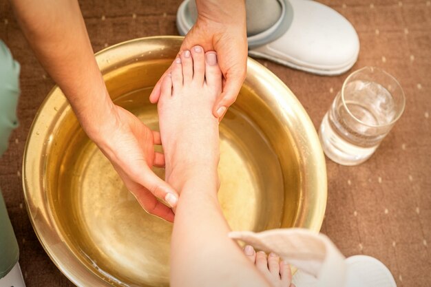 Washing female foot in a special container by male masseur in spa salon.