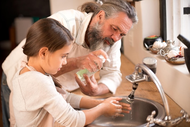 Washing the germs away Shot of a girl washing her hands in the kitchen sink as her grandfather stands by