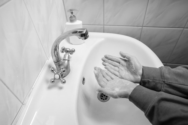 コロナウイルス予防のために石鹸男で手をこすりながら手を洗う白黒写真