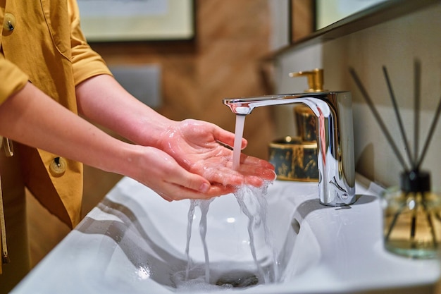 Washing hands under running water from faucet in washbasin