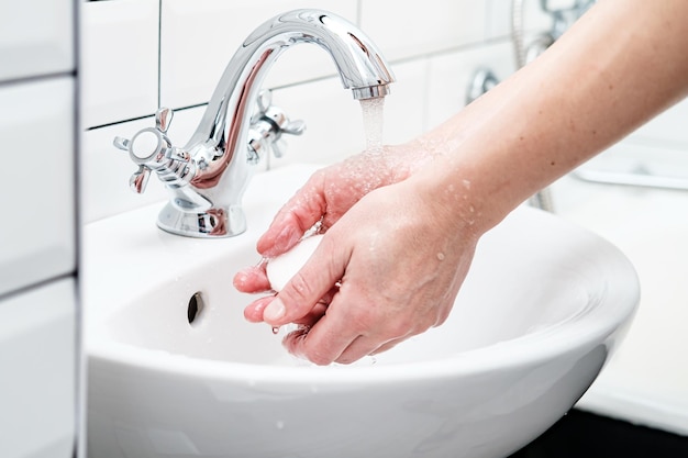 Washing hands with soap under running water in the bathroom