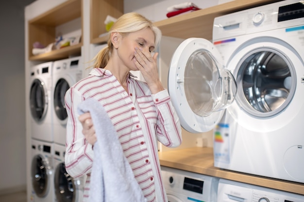 洗濯機。洗濯機の近くに立っている縞模様のシャツのブロンドの女性