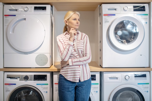 Washing machines. Blonde woman in striped shirt standing near washing machines