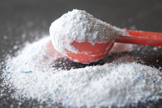 Washing powder in plastic spoon on black background top view