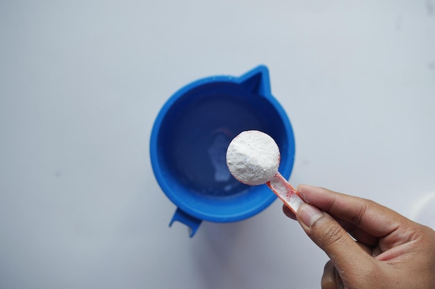 Washing powder in plastic spoon on black background top view