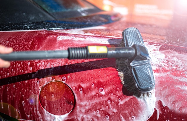 washing red car with brush and pressure washer