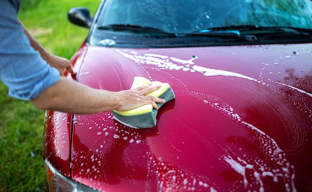庭で泡の入ったスポンジで赤い車を洗う。