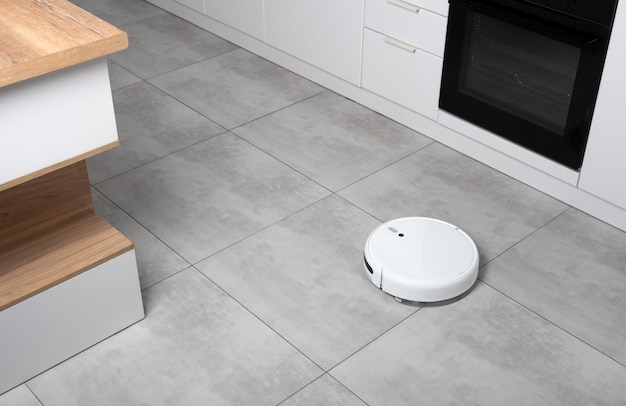 Washing White robot vacuum cleaner on a concrete tile floor cleaning dust in a Scandinavian loft minimalist kitchen interior. Smart Electronic Household Technology