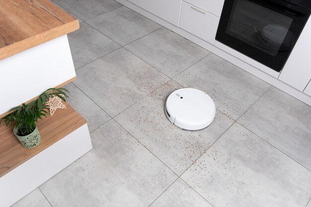 Washing White robot vacuum cleaner on a concrete tile floor cleaning dust in a Scandinavian loft minimalist kitchen interior. Smart Electronic Household Technology