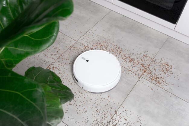 Washing White robot vacuum cleaner device cleaning floor from crumbs groats at home on utonite tiles in the kitchen.