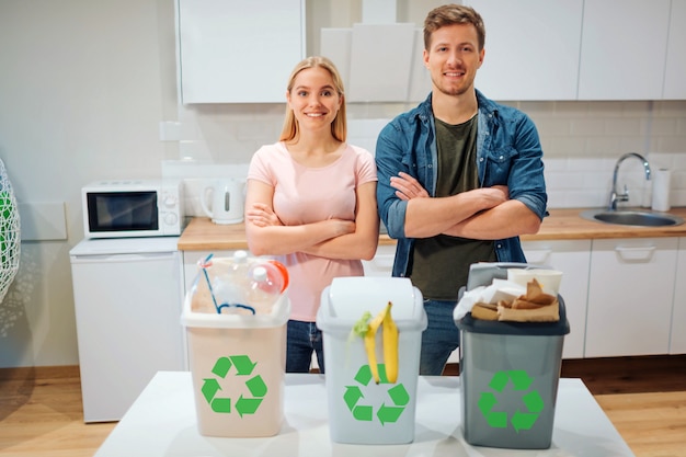 Waste sorting at home. Protect the environment. Young happy family put waste in colorful garbage bins with green recycling icon in the kitchen