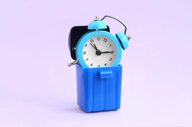 Wasting time concept. Alarm clock in trash bin