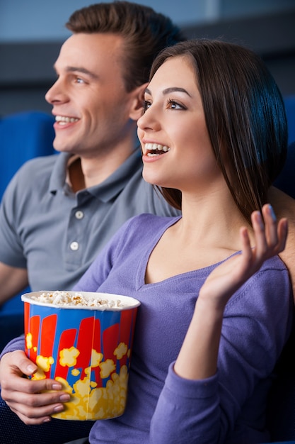 Wat een spannende film! Zijaanzicht van een gelukkig jong stel dat popcorn eet tijdens het kijken naar een film in de bioscoop