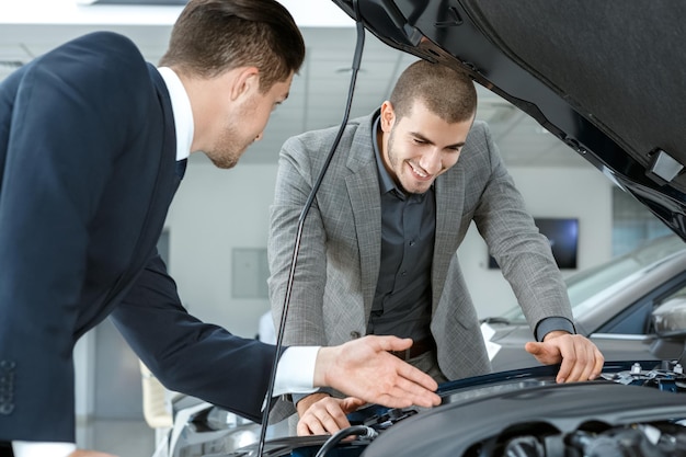 Wat een uitzicht Vrolijke zakenman en een autodealer die samen de motor van een nieuwe auto controleren