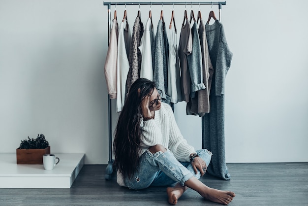 Foto wat moet ik dragen? doordachte jonge vrouw in vrijetijdskleding zittend op de vloer thuis