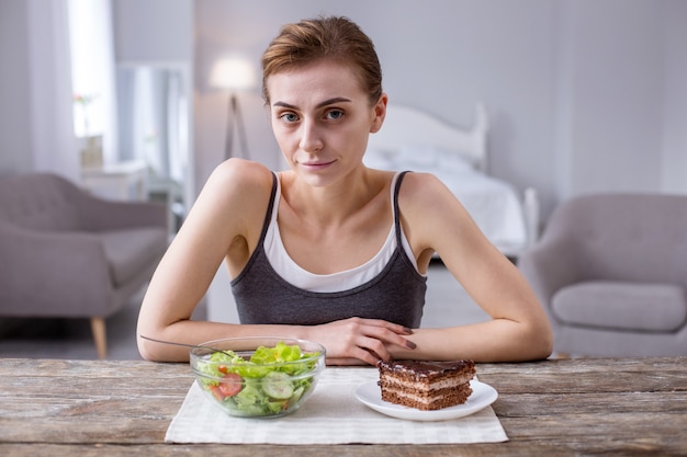 Wat te kiezen. Aangename aardige vrouw die aan tafel zit terwijl ze naar je kijkt