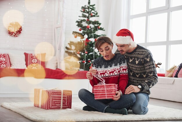 Wat zit daar in. Man verrast zijn vrouw voor Kerstmis in de mooie kamer met decoraties voor de feestdagen