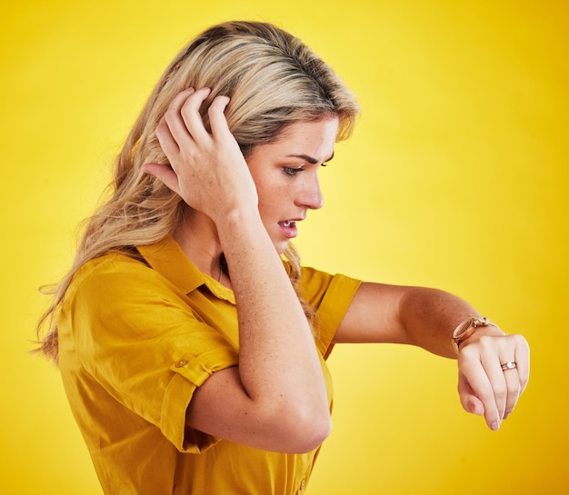 Watch late and woman checking the time in a studio with a shock scared and surprise face expression Panic anxiety and confused female model with a wristwatch isolated by a yellow background