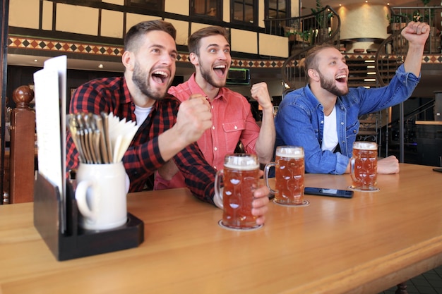 Guardare il calcio al bar. amici felici che bevono birra e fanno il tifo per la squadra del cuore, celebrando la vittoria.