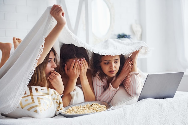 Guardare film di paura. felici amiche che si divertono al pigiama party in camera da letto.