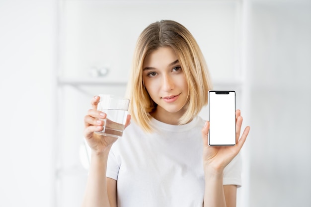 Water app hydratatiedieet gezond lichaam mooie frisse vrouw met glas met behulp van telefoon met schermmodel op intreepupil lichte achtergrond