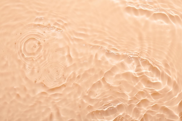水ベージュ表面の抽象的な背景泡と化粧品のアクア保湿剤の波と波紋のテクスチャー