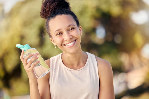 Water bottle fitness and nature of black woman in portrait for outdoor exercise wellness and healthy diet lifestyle in park or forest Trees bokeh workout and sports girl with drinking water gear