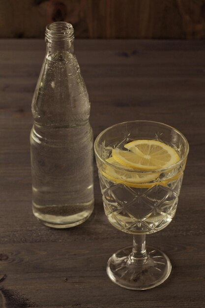 Foto bottiglia d'acqua e bicchiere d'acqua con limone su un tavolo di legno scuro