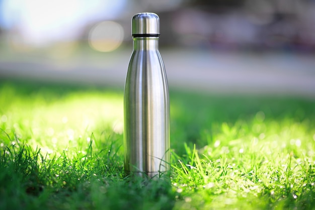 Water bottle on green grass steel thermo water bottle of silver on background of blurred grass