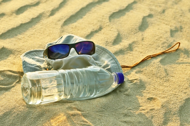 Water bottle, hat and sunglasses lying on the sand in the desert. survival in the heat of the desert