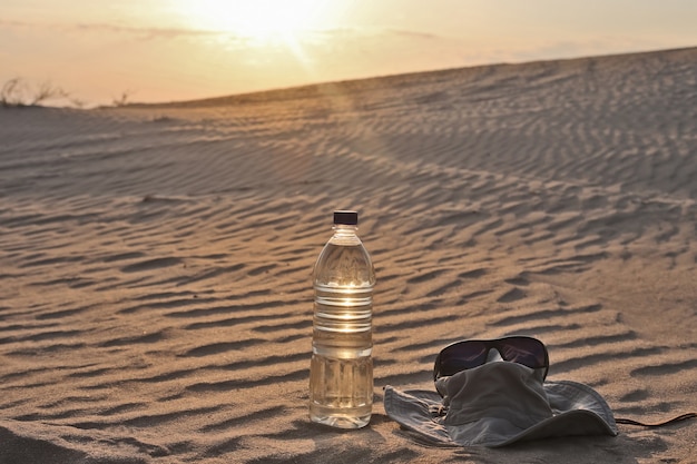 Water bottle, hat and sunglasses lying on the sand in the desert