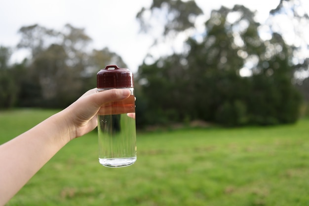 A water bottle held by a female hand on nature background.