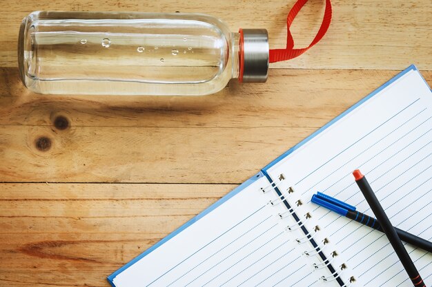 Water bottle, an opened notebook and pens on wooden table