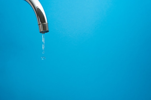 Water coming out of a tap on blue background. Whith copyspace