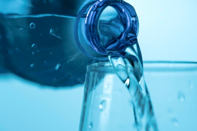 Water dat uit een plastic fles in een glazen beker op een blauwe achtergrond stroomt