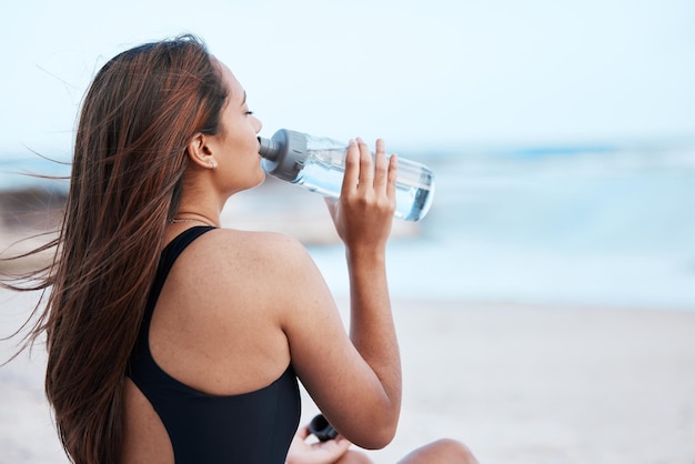 のどが渇いて水を飲むと、ビーチで女性がリラックスして休日の平和とハワイの海で禅 水分補給の穏やかさと夏の旅行休暇のために海でボトルから飲む女の子